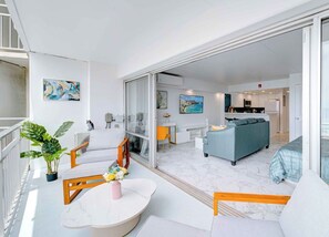 A modern living room with a sofa, a dining table with chairs, and a kitchen area in the background. - Renovated Beach View Condo, Fireworks, Waikiki (Honolulu)