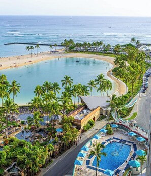 A resort with a large pool, palm trees, and a beach. - Renovated Beach View Condo, Fireworks, Waikiki (Honolulu)