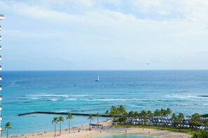 A beach with palm trees, a sandy shore, and a view of the ocean with sailboats. - Renovated Beach View Condo, Fireworks, Waikiki (Honolulu)