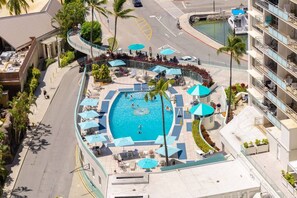 A rooftop pool area with a swimming pool, lounge chairs, umbrellas, and a view of the surrounding buildings. - Lux Beach View Condo, Open 1BR, Waikiki (Honolulu)
