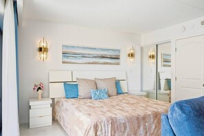 A bedroom with a bed, bedside tables, a mirror, and a painting on the wall. - Lux Beach View Condo, Open 1BR, Waikiki (Honolulu)