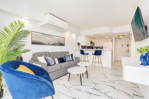 Una sala moderna con un sofá gris, un sillón azul y una zona de comedor con taburetes de bar.