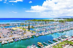 A marina with numerous boats docked, a parking area, and a clear view of the ocean. - Ocean & Marina Sunset Condo, Free Parking, Waikiki (Honolulu)