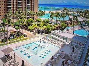 A resort with a large pool, palm trees, and a view of the beach. - Ocean & Marina Sunset Condo, Free Parking, Waikiki (Honolulu)