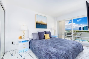 Ein modernes Hotelzimmer mit einem großen Bett, Blick auf die Stadt und einem Balkon mit Sitzgelegenheit.