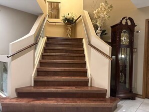 A wooden staircase with a handrail, leading to a landing with a vase of flowers and a clock.