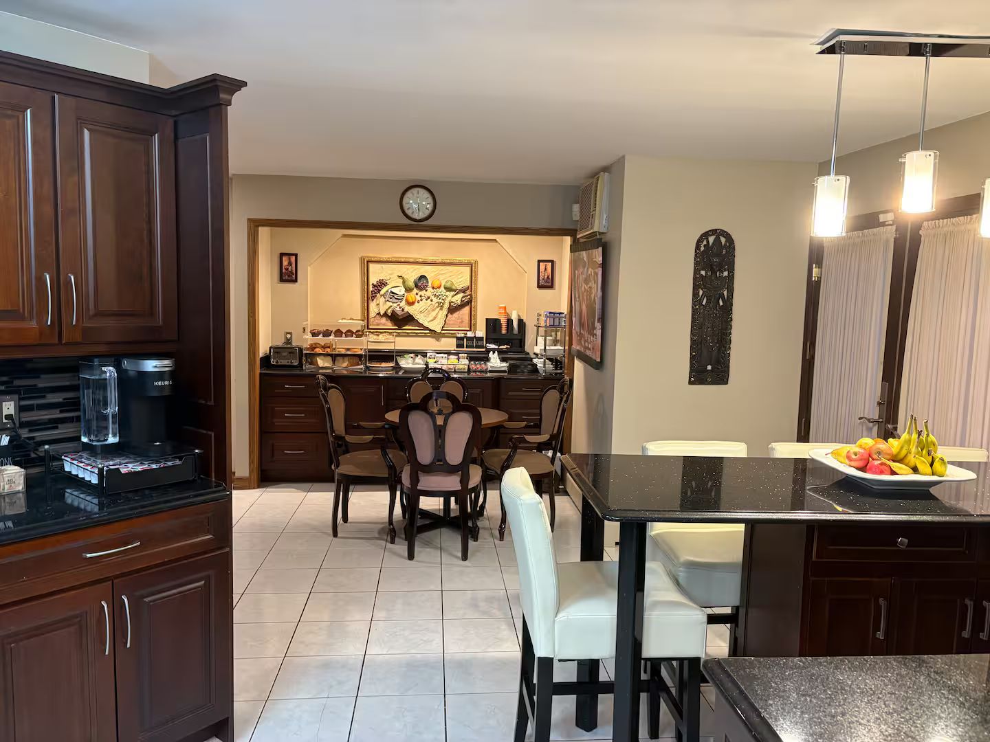 A kitchen with dark wooden cabinets, a coffee machine, a dining area with a table and chairs, and a fruit bowl on the island.