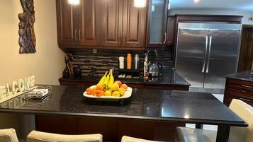 A modern kitchen with dark wood cabinets, a stainless steel refrigerator, and a fruit bowl on the island.