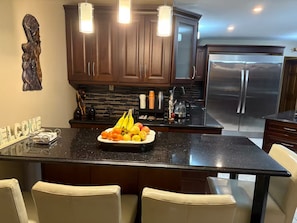 A modern kitchen with dark wood cabinets, a stainless steel refrigerator, and a fruit bowl on the island.