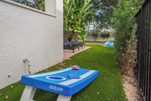 Una mesa de ping pong GoSports en un patio con césped artificial, una pared blanca y una cerca negra.