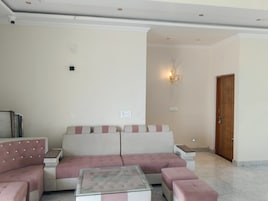 Sala de estar com sofá, pufes, mesa de centro de vidro e uma porta.