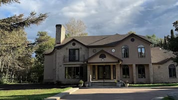 A large, two-story stone house with a symmetrical facade, a central entrance with a covered porch, and a driveway leading to the front door.
