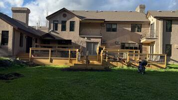 A residential building with multiple levels, a covered porch, and a grassy yard.