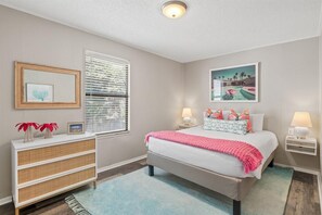 A bedroom with a bed, bedside tables, a dresser, a window with blinds, and a wall-mounted picture. - Dogwood Bungalow (Santa Rosa Beach)