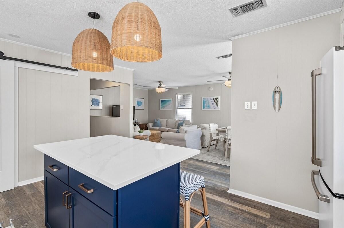 A modern kitchen with a central island, pendant lighting, and a refrigerator.