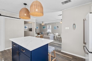 A modern kitchen with a central island, pendant lighting, and a refrigerator. - Dogwood Bungalow (Santa Rosa Beach)