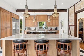 A spacious kitchen with a large island, wooden cabinets, and three bar stools. - Kuenemann Estate - Pool Table & Poker Room (Fredericksburg)