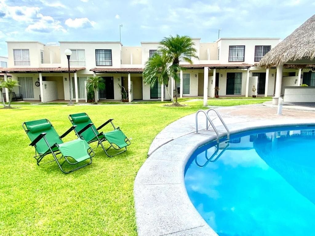 Una piscina con borde transparente, rodeada por una zona ajardinada con sillas de descanso.