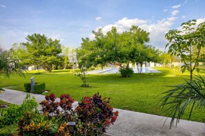 A well-maintained garden with a swimming pool, surrounded by lush greenery and a clear sky.