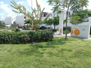 Una zona verda amb un edifici blanc, arbres i una paret amb cercles taronja.