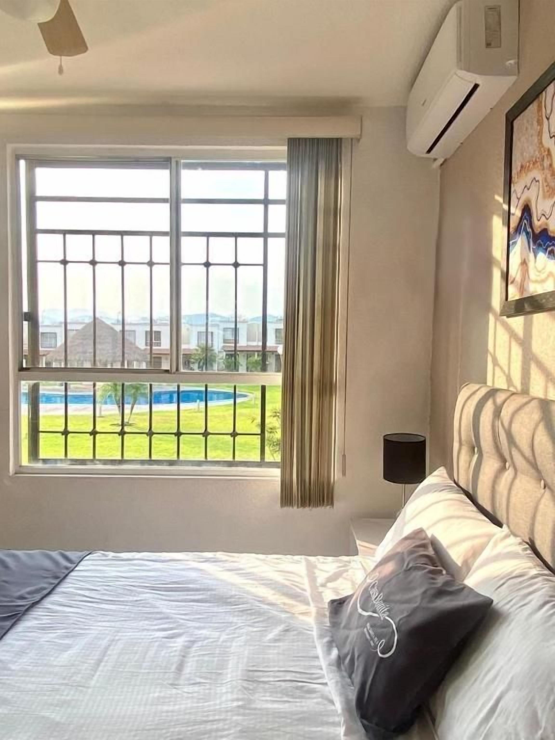 Habitación de hotel con una cama, ventana con vistas a una piscina y montañas, y aire acondicionado.