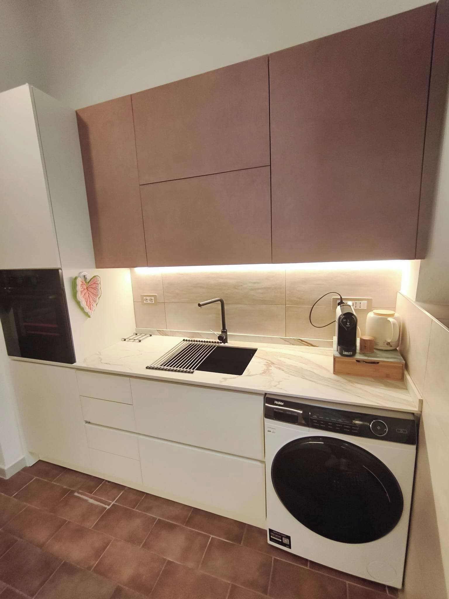 Cocina compacta con lavavajillas integrado, un lavamanos y una cafetera.