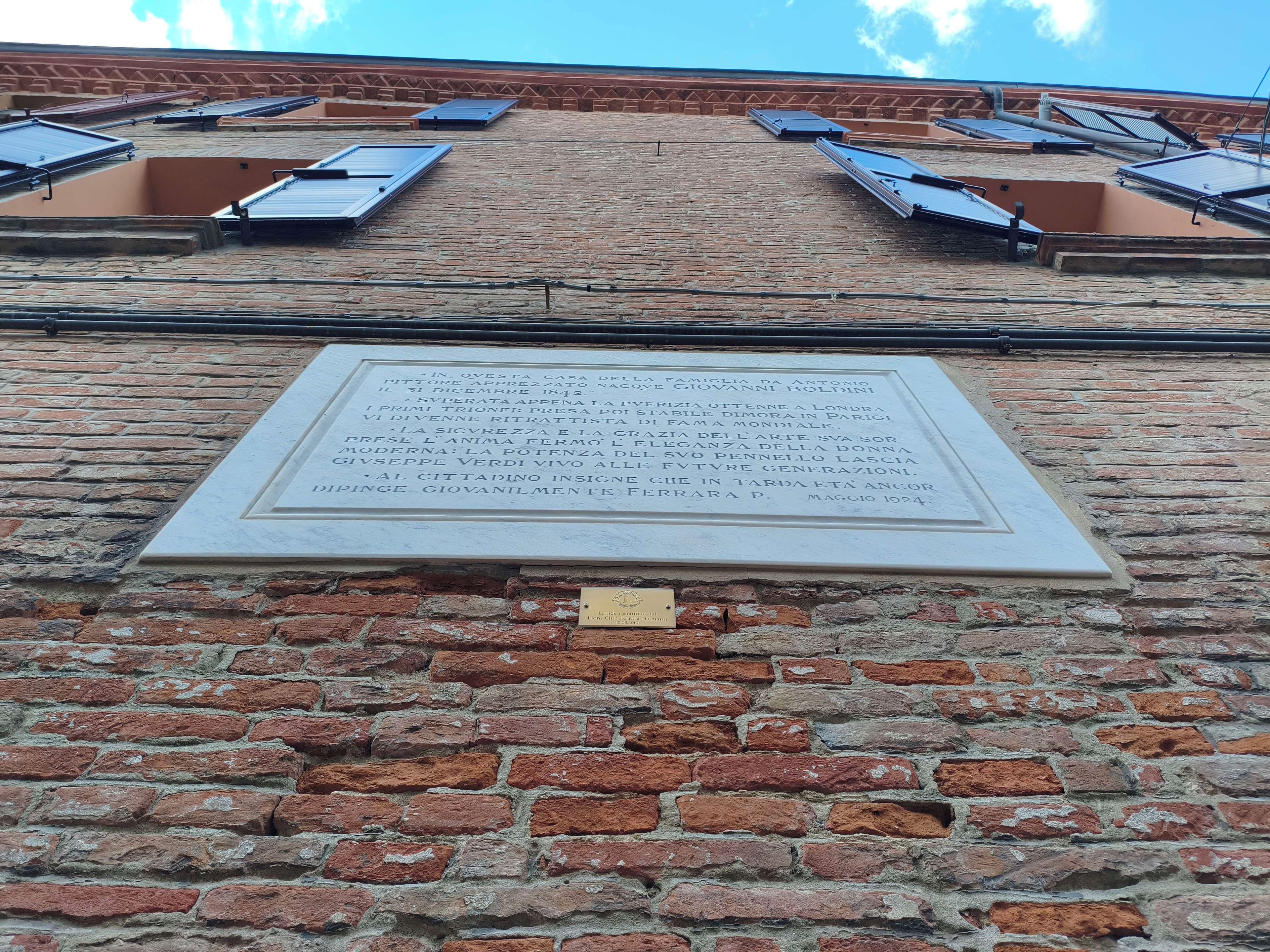 Eine Ziegelwand mit einer Gedenktafel und Solaranlagen auf dem Dach.