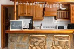Une cuisine avec des meubles de rangement en bois, un mur en pierre, un panneau noir, des verres à vin et une bouteille.