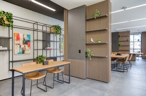 A modern office space with a wooden table and chairs, a bookshelf with plants, and a colorful abstract painting. - Nik Paulista (São Paulo)