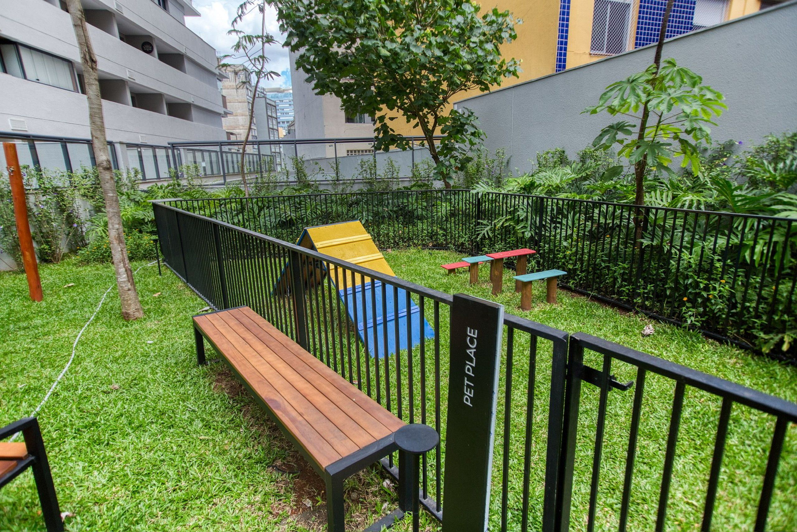 Un espace extérieur clôturé comprenant un banc en bois, une structure de jeu jaune et un panneau indiquant « ESPACE POUR ANIMAUX ».