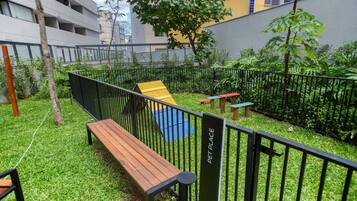 Un espace extérieur clôturé comprenant un banc en bois, une structure de jeu jaune et un panneau indiquant « ESPACE POUR ANIMAUX ».