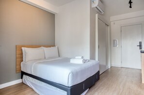 A hotel room with a bed, a wooden headboard, a white wall, a door, and a small window. - Nik Paulista (São Paulo)