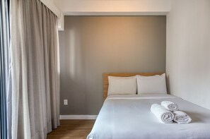 Habitación de hotel con cama, cabecera y ventana con cortinas.