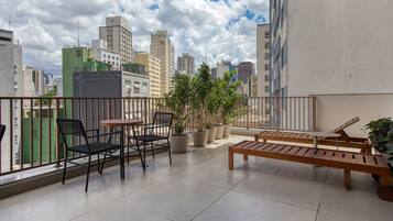 Un balcon offrant une vue sur les toits de la ville, avec une table, des chaises et des plantes en pot.