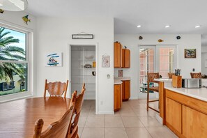 A modern kitchen with wooden cabinets, a dining area with a wooden table and chairs, and a view of palm trees outside. - Salty Smiles (Treasure Island)