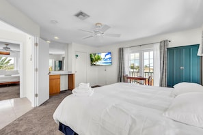 A hotel room with a large bed, a desk, a television, and a balcony with a view. - Salty Smiles (Treasure Island)