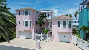 A pink two-story building with a white fence, a garage, and a staircase leading to a balcony. - Salty Smiles (Treasure Island)