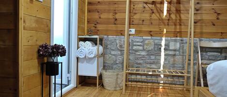 A wooden-paneled room with a wooden drying rack, a stone wall, a white towel rack, and a black floor lamp.