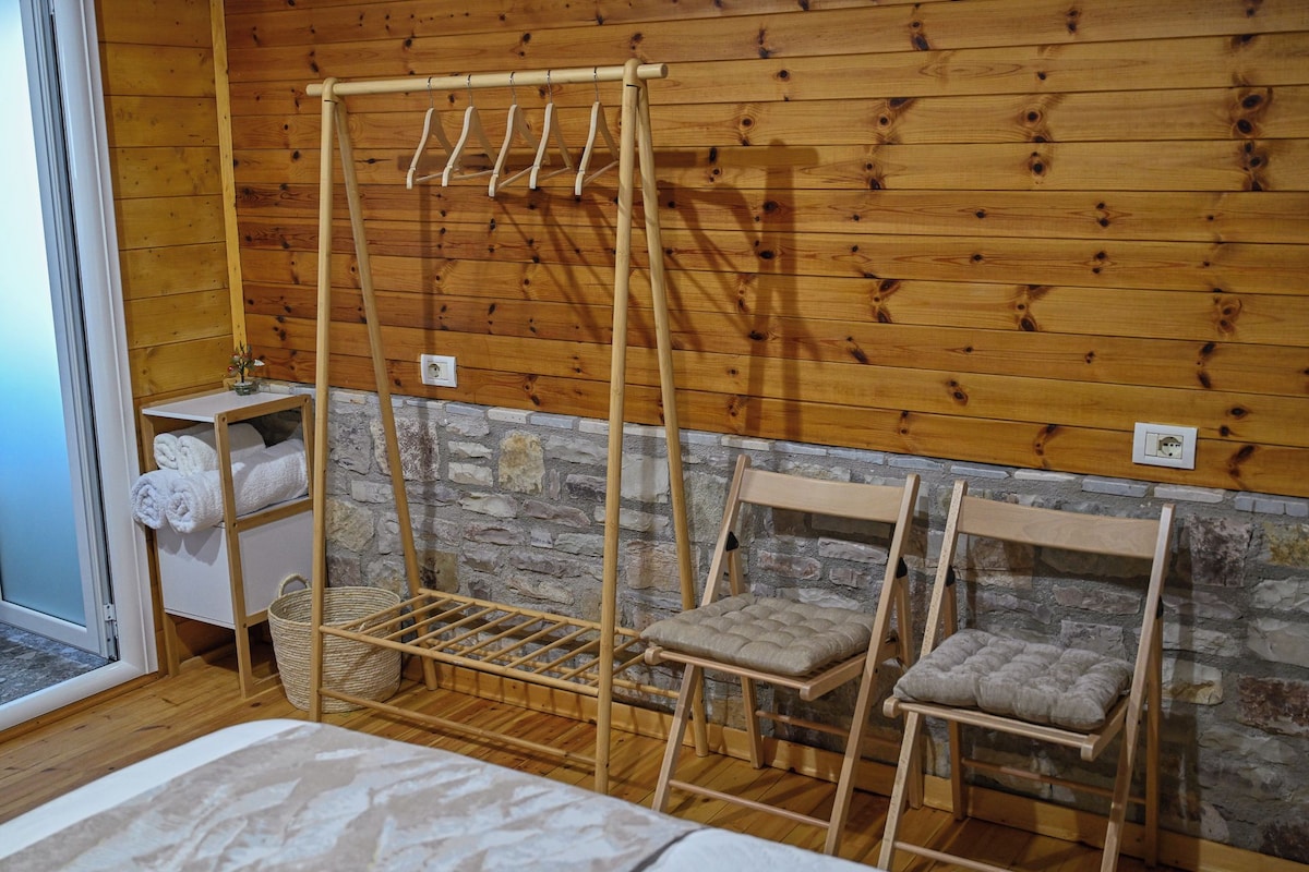 A wooden room with a bed, a wooden drying rack, a stone wall, and a small table with towels.