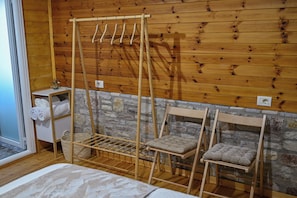A wooden room with a bed, a wooden drying rack, a stone wall, and a small table with towels. - Airport comfort nest (Kamëz)