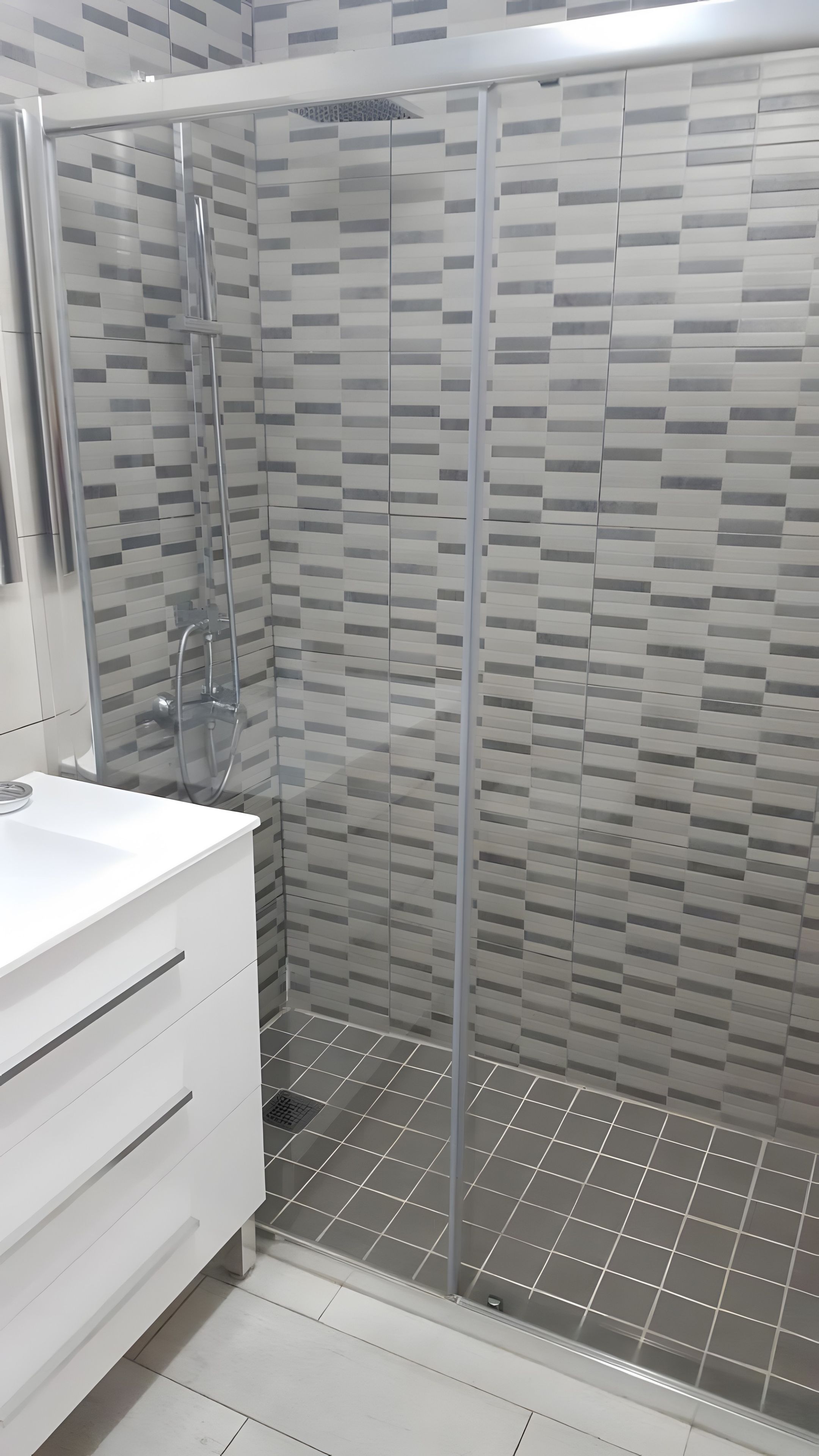 A modern bathroom with a shower enclosure, a white vanity, and a tiled floor.