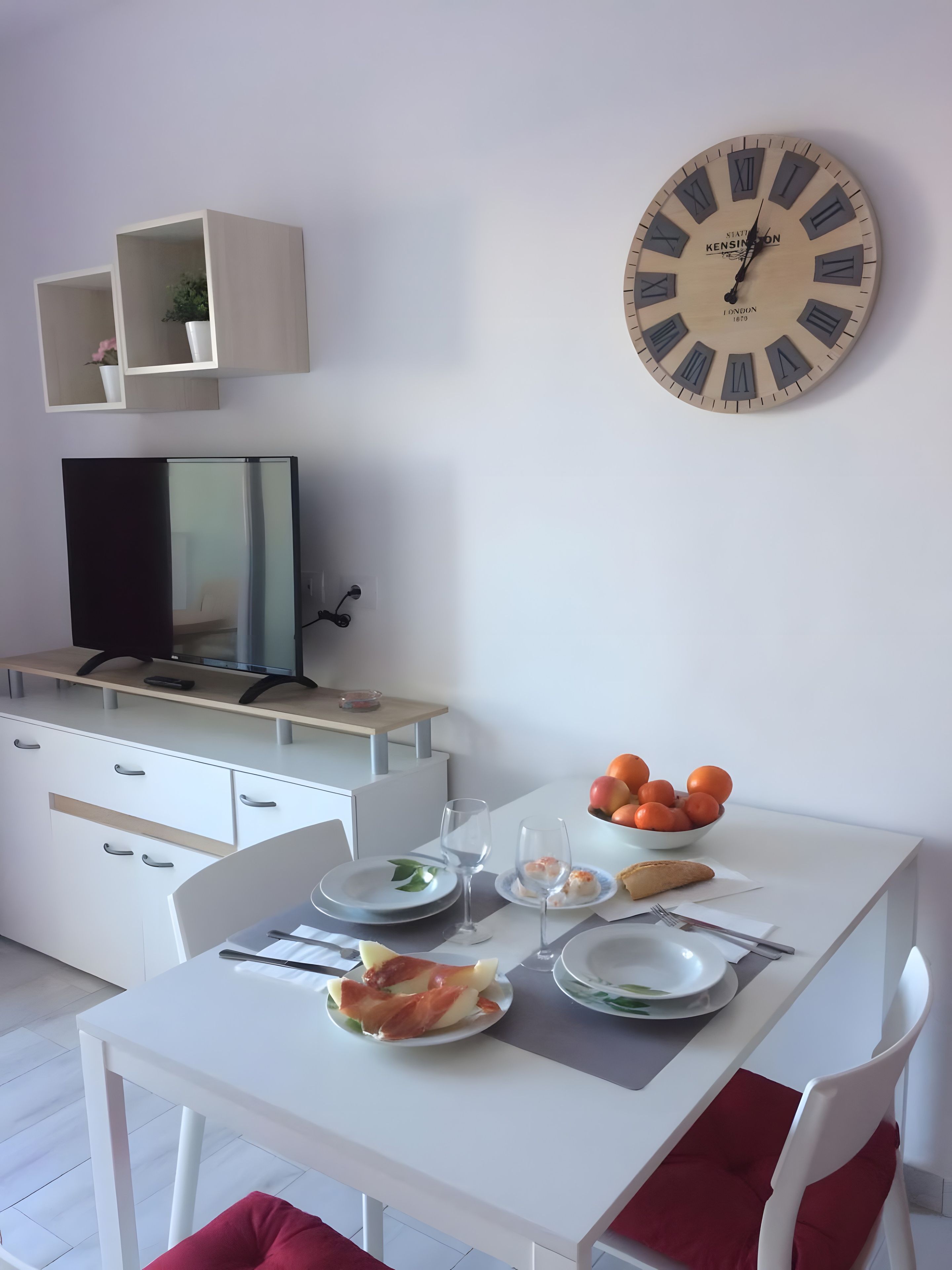 A dining area with a white table, chairs, and a clock on the wall.