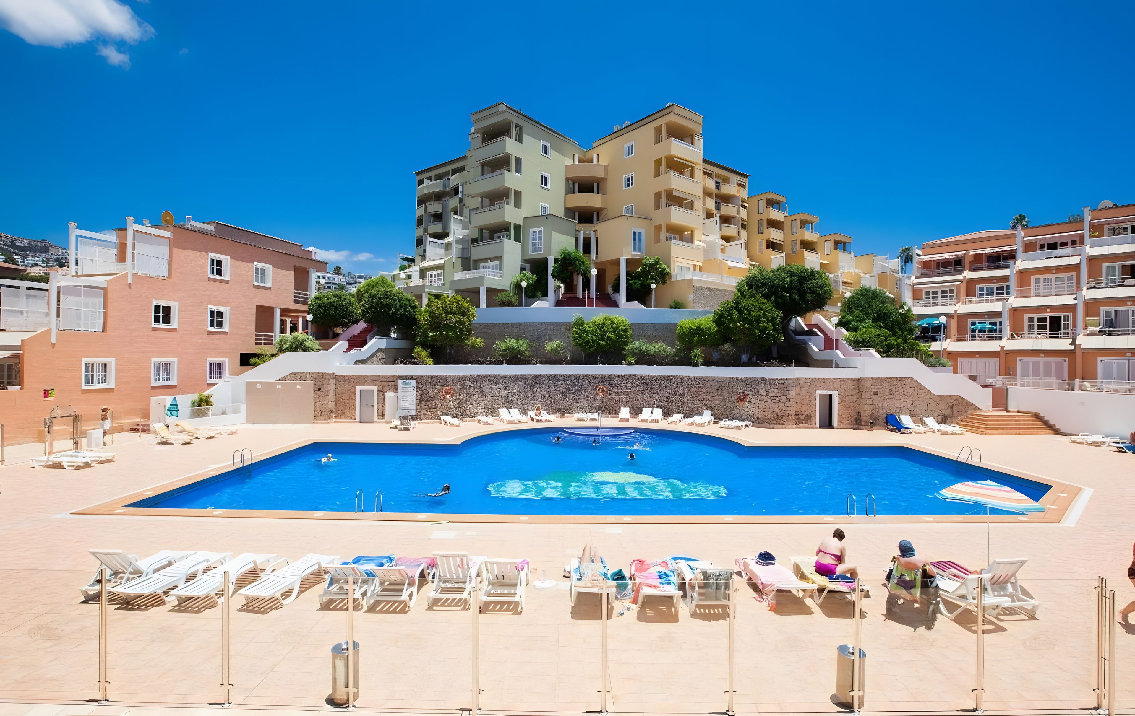 A swimming pool with sun loungers and a view of multi-story buildings.