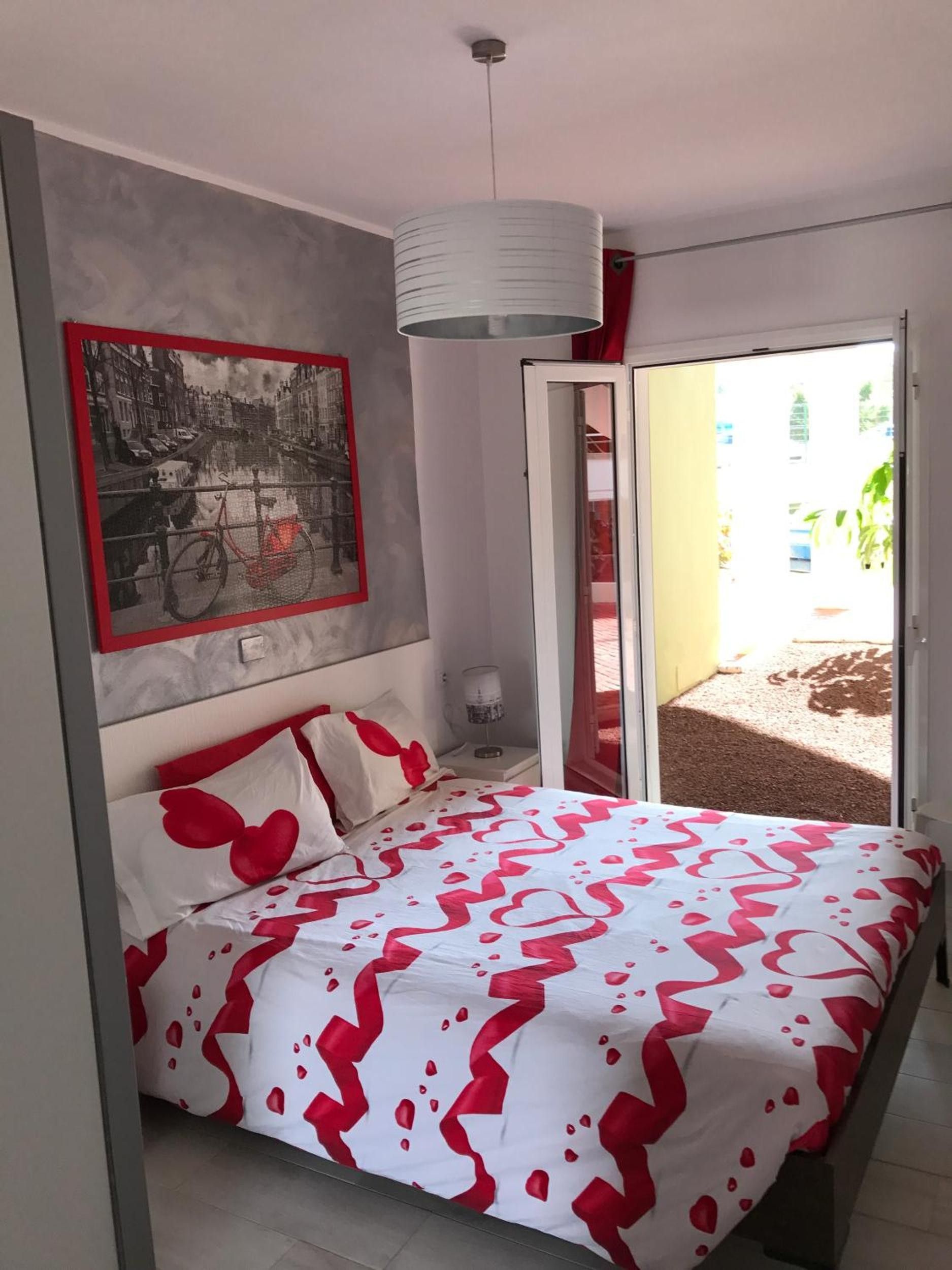 A bedroom with a bed, a nightstand, a lamp, a framed picture, and a sliding glass door leading to an outdoor area.