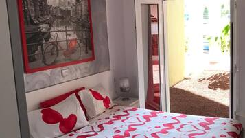 A bedroom with a bed, a nightstand, a lamp, a framed picture, and a sliding glass door leading to an outdoor area.