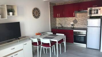A modern kitchen with red cabinets, a microwave, and a dining area with a white table and chairs.