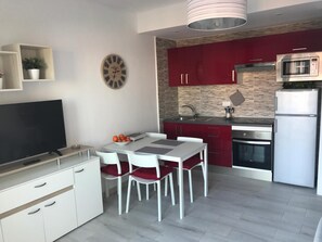 Una cocina moderna con armarios rojos, un microondas y un comedor con mesa y sillas blancas.