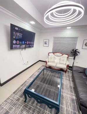 Ein modernes Wohnzimmer mit einem an der Wand montierten Flachbildfernseher, einem Glastisch, einem weißen Ledersessel und einem schwarzen Ledersofa.
