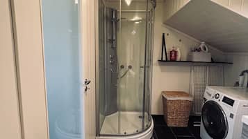 Een douchehoek met glazen deuren, een wasmachine en een wasmand in een kleine badkamer.