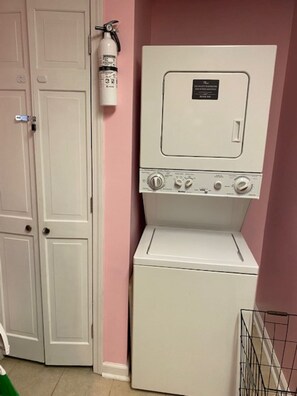 A laundry room with a front-loading washer and dryer, a fire extinguisher mounted on the wall, and a closed door. - Enjoy the pool, relax by the fire pit, or spend time exploring North Georgia! (Oakwood)